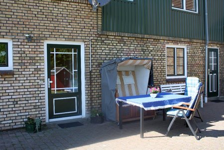 Eingangsbereich mit Gartenmöbeln. Haus mit hellem Stein und grün weißen Fenstern und Türen. 