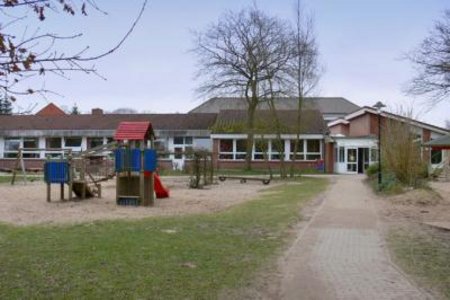Außenbereich der Kita Schuby mit Spielturm und Sandkiste. Im Hintergrund der Eingangsbereich. 