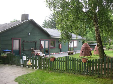 Eingangsbereich der Kita Schneckenhaus in Ellingstedt. Grüne Fassade mit braunen Fenstern. Davor ein grüner Zaun.